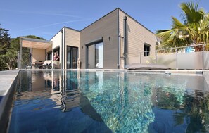 Una casa moderna con piscina, ampie finestre e un'area salotto esterna coperta.