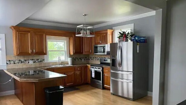 A modern kitchen with wooden cabinets, a stainless steel refrigerator, and a large island with a sink. - 3bed 2bath nestled in cozy Grandview neighborhood (pet friendly!) (Dubuque)