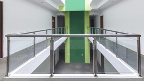 Un pasillo interior moderno con barandillas de vidrio, un pilar central verde y una escalera que sube.