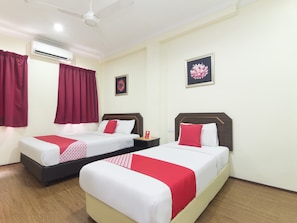 A hotel room with two beds, each with white bedding and red accents, a ceiling fan, an air conditioning unit, and a framed floral artwork on the wall. - OYO 327 Buddys Hotel (Kuala Lumpur)