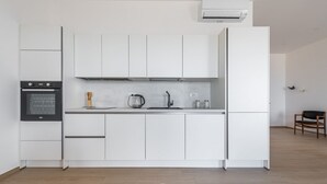 Una cucina moderna con mobili bianchi, forno a incasso, macchina del caffè e frigorifero.