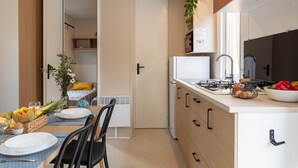 A compact kitchen with a stove, sink, and cabinets. There is a dining area with a table set for two, a chair, and a vase of flowers. - Le Palmier, mobile home not overlooked (Hyères)