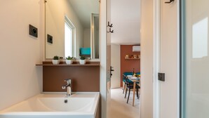 A modern bathroom with a large sink and mirror, a small window, and a door leading to a dining area. - Le Palmier, mobile home not overlooked (Hyères)