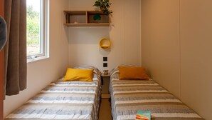 A small, cozy room with two beds, a window, a plant, and a shelf with a plant and a decorative item. - Le Palmier, mobile home not overlooked (Hyères)