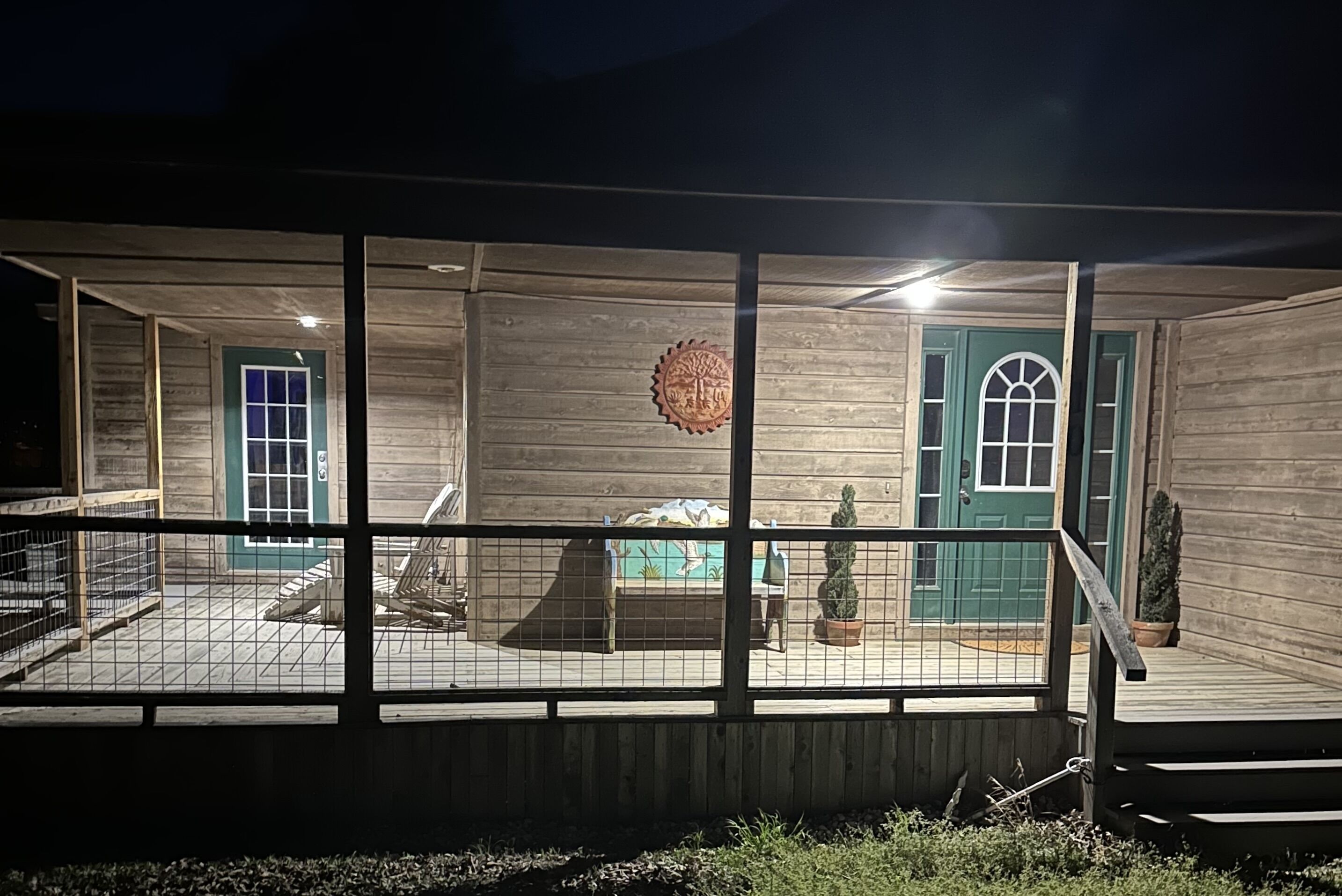 Una cabaña de madera con un deck cercado, dos puertas y un pequeño jardín.