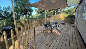 A wooden deck with a table and chairs, surrounded by a bamboo fence, and a large shade sail overhead. - Le Cycas, a new mobile home with sea view (Hyères)