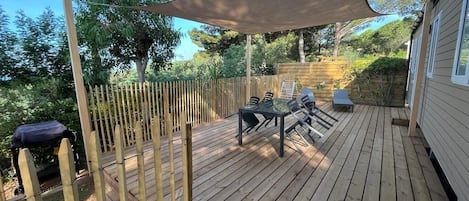 A wooden deck with a table and chairs, surrounded by a bamboo fence, and a large shade sail overhead.
