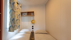 Ett litet, kompakt sovrum med två enkelsängar, ett sängbord med en lampa och en hylla med dekorativa föremål.