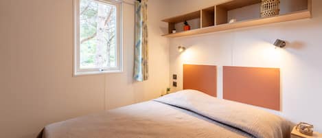 Une chambre à coucher avec un lit, une fenêtre avec des rideaux, une étagère avec des objets décoratifs et des lampes fixées au mur.