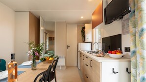 Een moderne keuken met een eethoek, een flatscreen televisie boven de aanrecht en een raam met gordijnen.