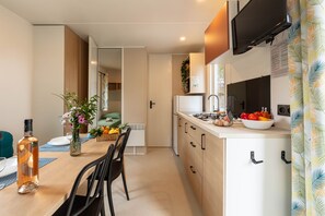 Eine moderne Küche mit Essbereich, einem flachbildfernseher über der Arbeitsfläche und einem fenster mit Vorhängen.