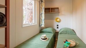 Een kleine, gezellige kamer met twee eenpersoonsbedden, een raam met uitzicht op bomen, een plankje met een hoed en een wandlamp.
