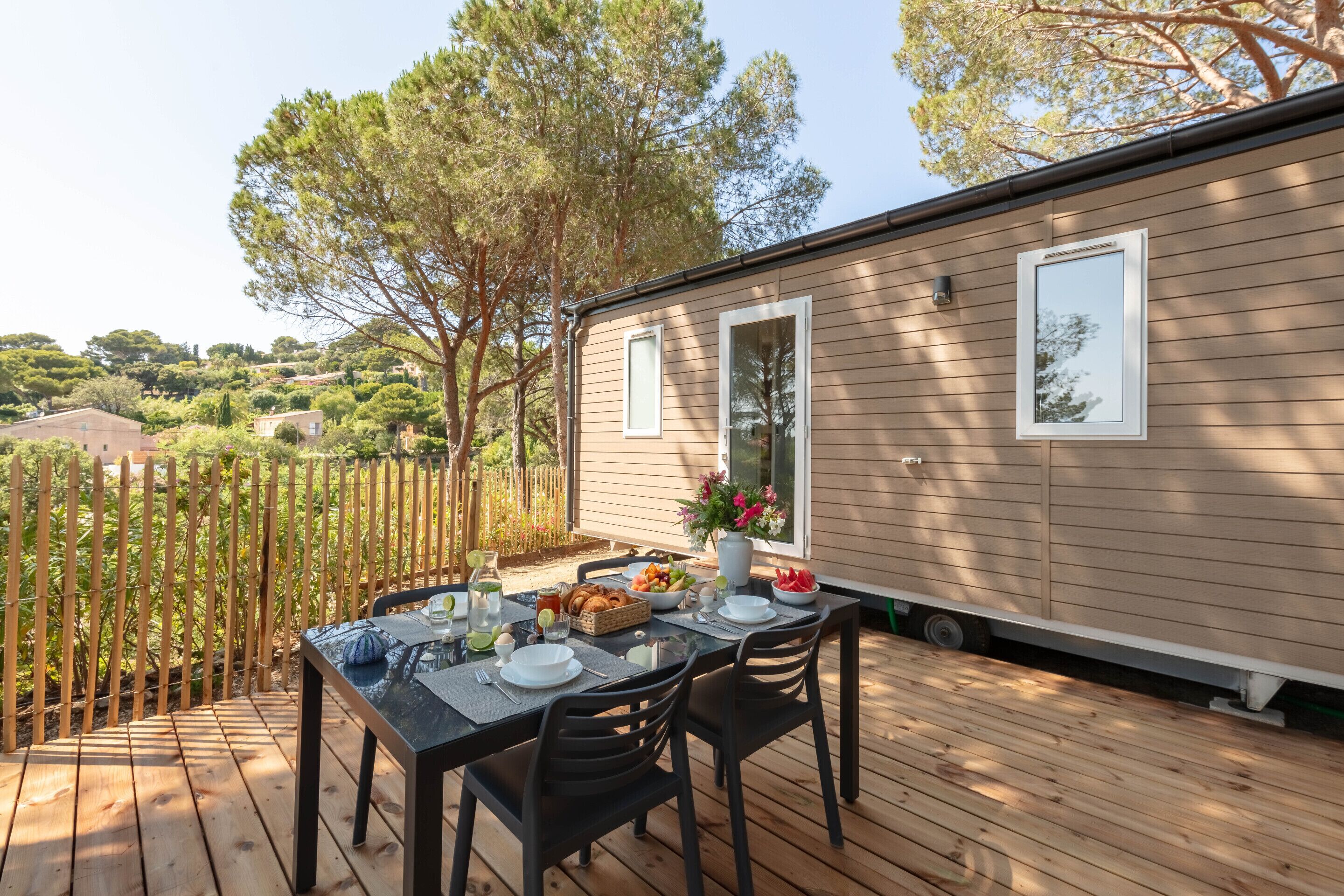 A deck with a table set for dining, overlooking a residential area with trees and houses.