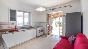 Une cuisine avec des meubles blancs, une cuisinière à gaz et un plan de travail rouge. Le salon est doté d’un canapé rouge agrémenté d’un coussin à motifs.