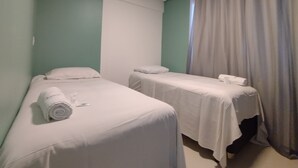 Et hotelværelse med to enkeltsenge, hver med en pude og et sammenrullet håndklæde.