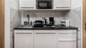 Eine kleine Küche mit weißen Schränken, einer schwarzen Arbeitsplatte, einer Mikrowelle, einer Kaffeemaschine und einem Wasserkocher.