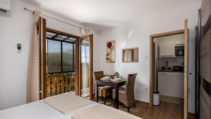 Ein Hotelzimmer mit Bett, Esstisch mit Stühlen, einer Küchenzeile und einem Balkon mit Blick.