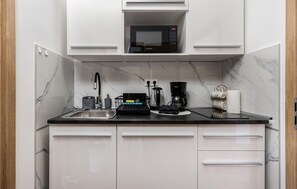 Eine kleine Küche mit weißen Schränken, einer schwarzen Arbeitsplatte, einer Mikrowelle, einer Kaffeemaschine und einem Wasserkocher.