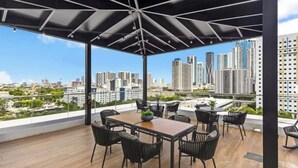 A rooftop terrace with a wooden table and chairs, a black umbrella, and a city view. - Vaca Rentalz Miami 1BR / 1BA Rooftop Pool (Miami)