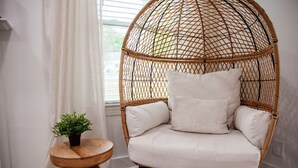 A wicker chair with cushions, a small wooden table with a plant, and a window with white curtains. - Beautifully Renovated and Decorated Home in Great Neighborhood (Augusta)