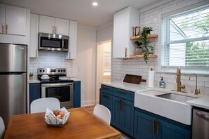 A modern kitchen with white and blue cabinetry, stainless steel appliances, and a window with blinds.