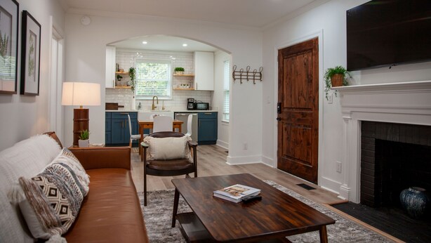 A living room with a sofa, coffee table, and fireplace. There is a kitchen in the background with a window and cabinets. - Beautifully Renovated and Decorated Home in Great Neighborhood (Augusta)