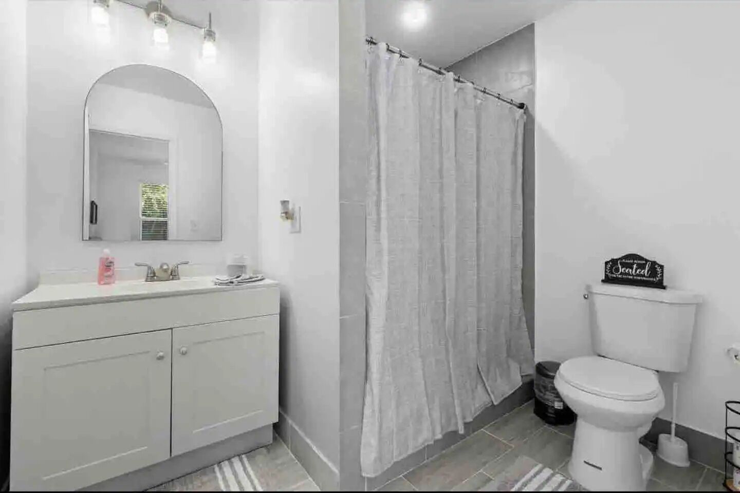 A bathroom with a white vanity, a large mirror, a toilet, and a shower curtain.