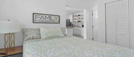 A bedroom with a floral bedspread, a bedside table with a lamp, and a framed sign on the wall that reads "FAMILY is life's greatest blessing."