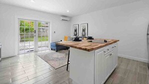 Une cuisine moderne avec des meubles blancs, un plan de travail en bois et une porte-fenêtre coulissante donnant sur une terrasse.