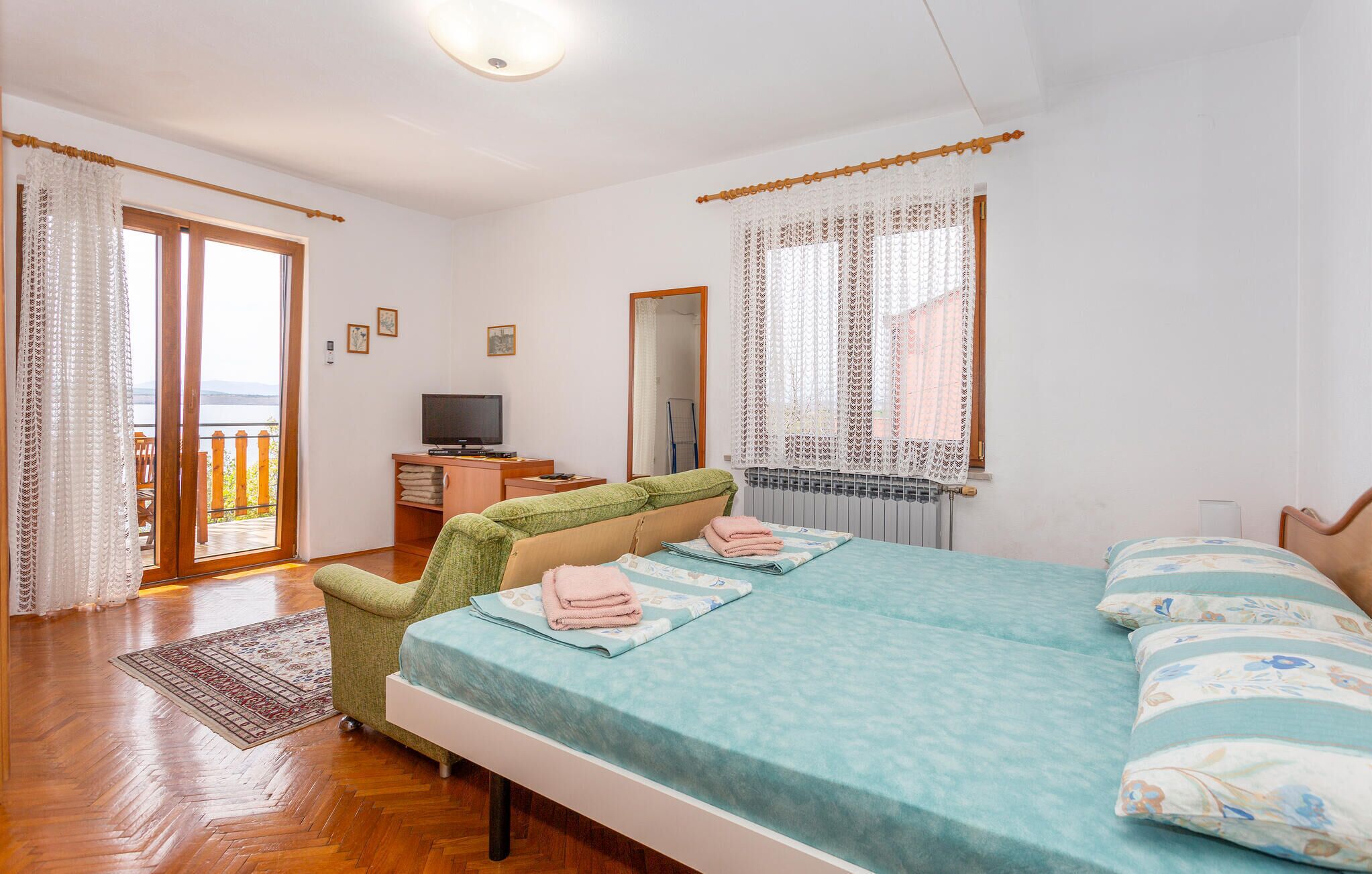 Une chambre à coucher avec un lit, une chaise, une télévision et une fenêtre avec des rideaux.