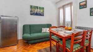Un espacio habitable compacto con zona de comedor, un sofá verde, una mesa de comedor de madera y un refrigerador.