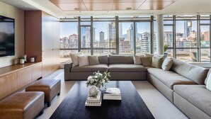 A modern living room with a large sectional sofa, a coffee table with books and a vase, and a city view through large windows. - Luxurious Penthouse in Trendy Yaletown with Private Rooftop Pool (Vancouver)