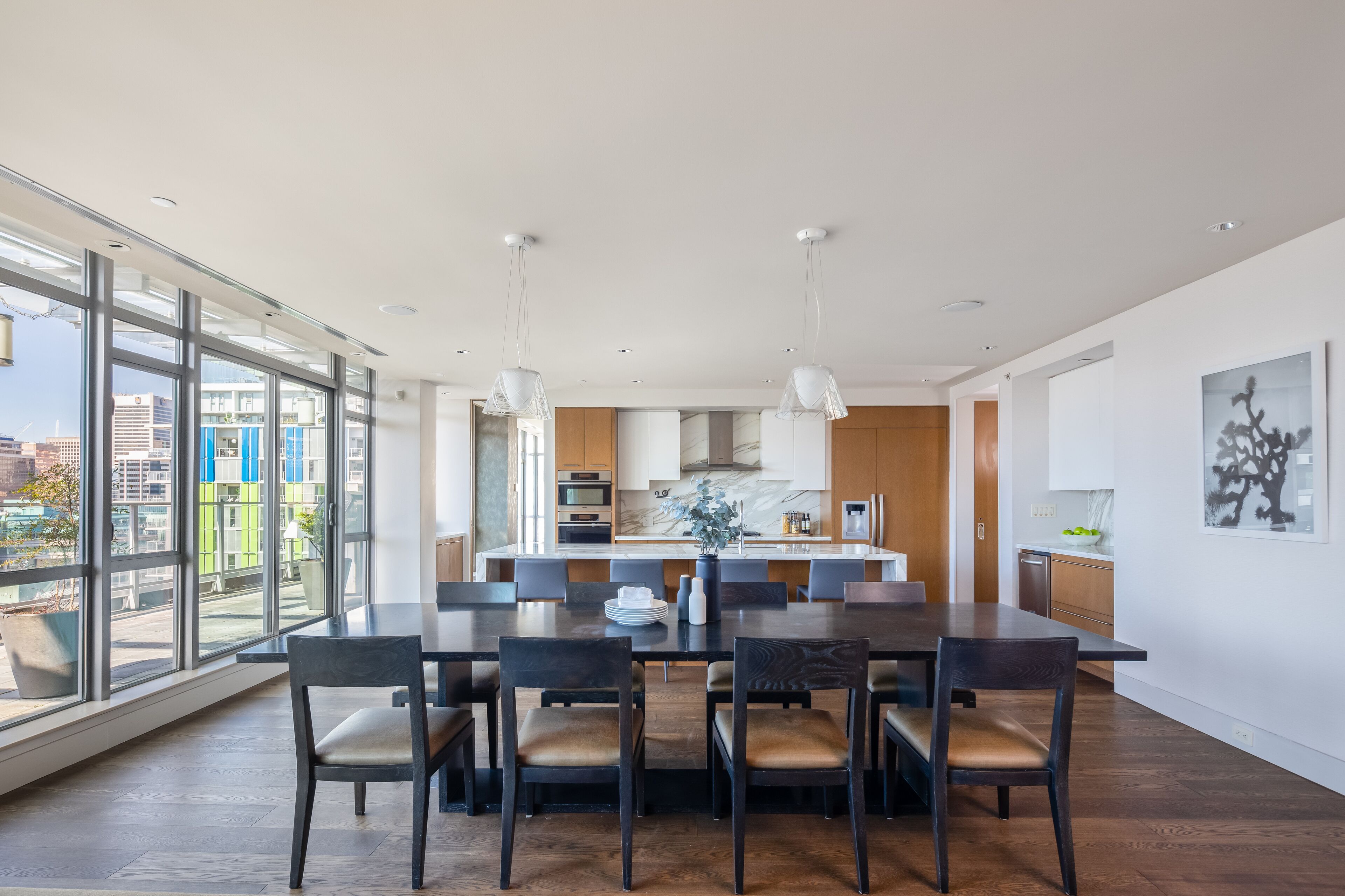 Una cocina moderna con una isla central, ventanas amplias y un comedor con mesa y sillas de madera oscura.