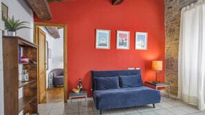 A room with a red wall, a blue sofa, a wooden bookshelf, and a small table with a lamp. - Seven House - Sweet Dreams in Florence (Firenze)