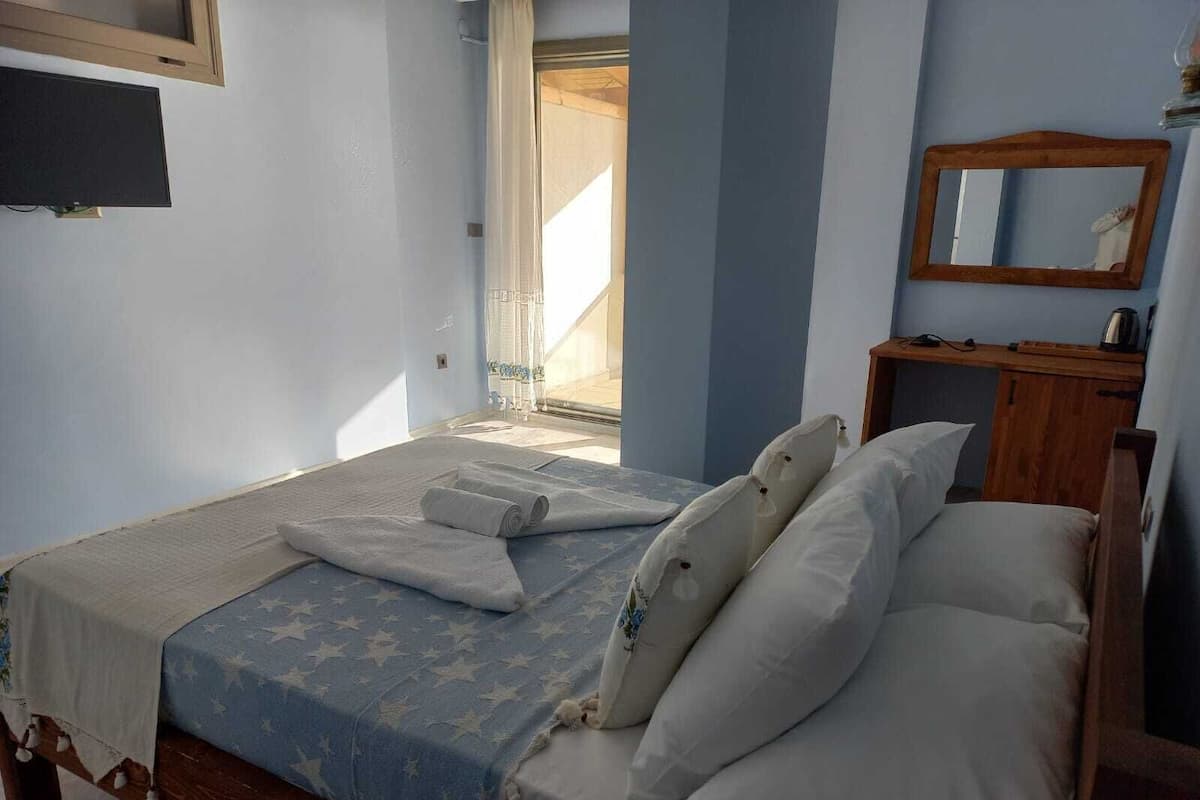 Ein Schlafzimmer mit einem Bett, einem Nachttisch aus Holz, einem Spiegel und einem Fenster.