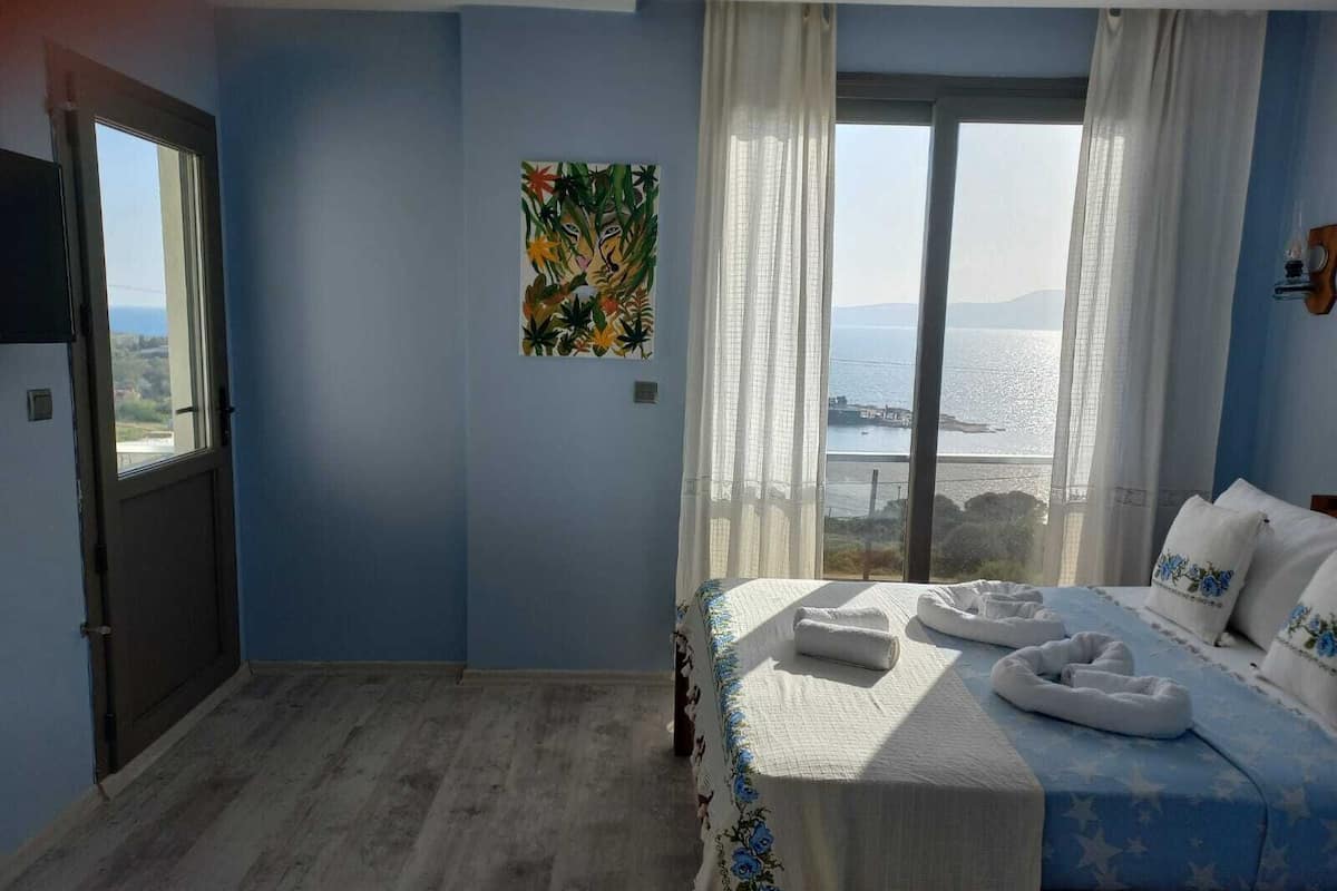 Ein Schlafzimmer mit Bett, Fenster mit Meerblick und einem Bild an der Wand.