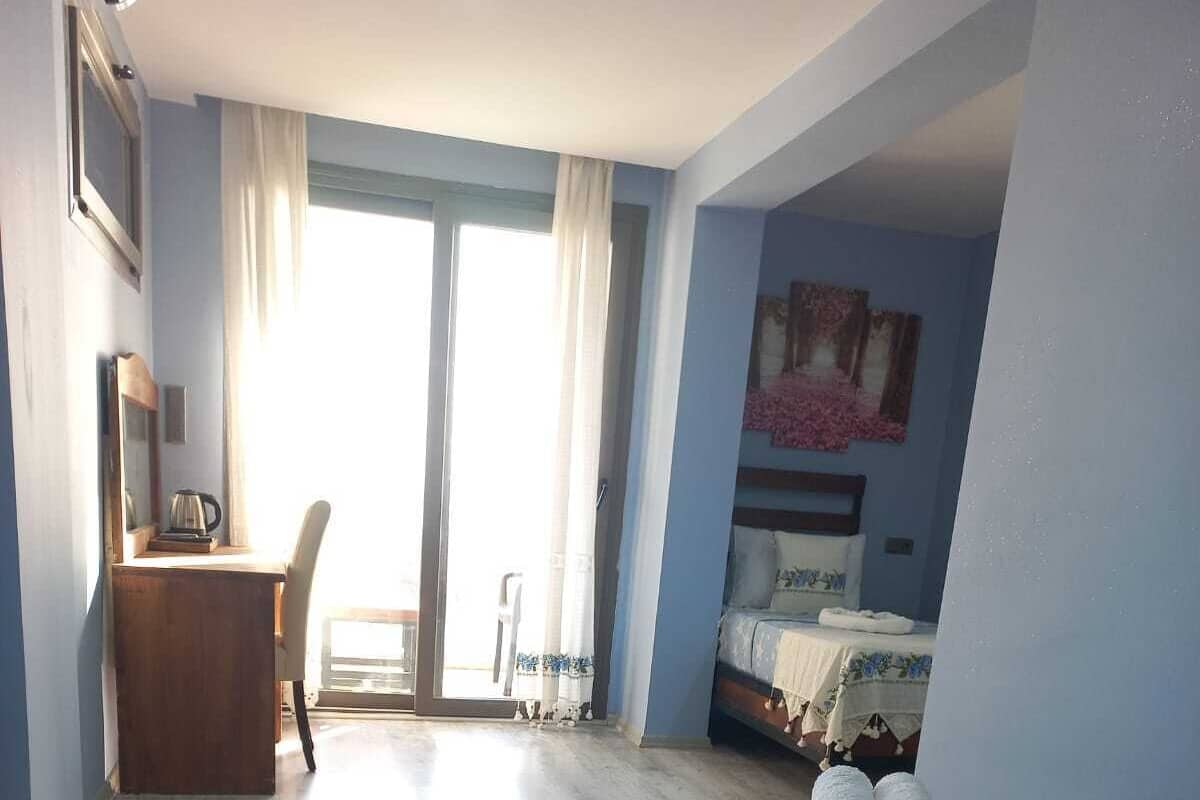 Ein Hotelzimmer mit einem Bett, einem Schreibtisch und einem Sessel. Ein Fenster mit Vorhängen bietet einen Blick ins Freie.