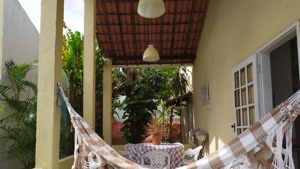 A hammock with macrame detailing, a checkered table, and potted plants in a covered outdoor area.