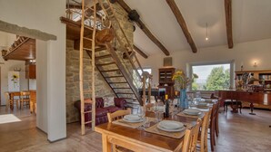 Un vaste espace dédié à la salle à manger, avec une table en bois dressée pour le repas, un escalier en pierre et une vue sur l’extérieur.