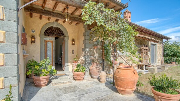 Un bâtiment en pierre doté d’une entrée rustique, de grands pots en terre cuite et d’une pergola recouverte de vignes.