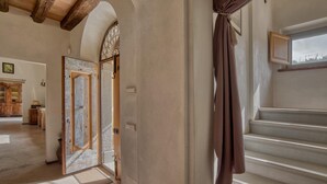 Un couloir avec une porte en bois, un escalier et une vue sur l’extérieur.