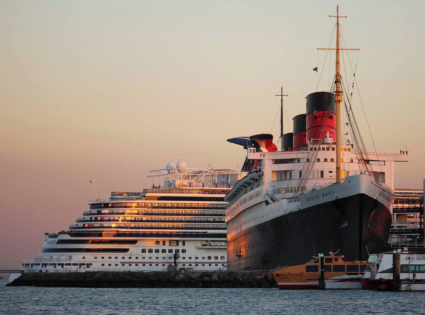 Een groot cruiseschip ligt aangemeerd in een haven, met meerdere dekken en een opvallende schoorsteen.