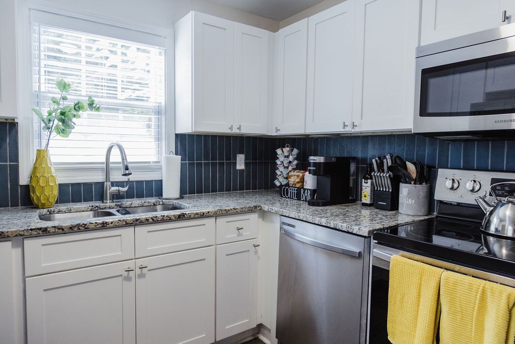 A modern kitchen with white cabinets, a stainless steel dishwasher, a black stove, and a microwave.