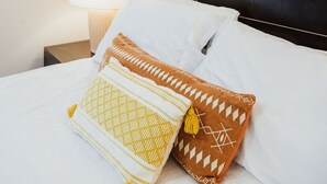Ein Hotelzimmer mit einem Bett, Kissen, einem Nachttisch, einer Lampe und einem runden Spiegel an der Wand.