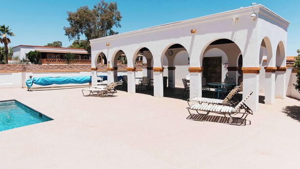 Un edificio con varios arcos y un área de piscina con sillones de descanso.