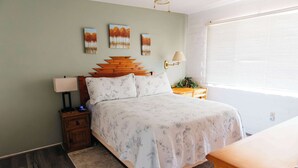 Un dormitorio con una cama, una mesita de noche con lámpara, cabecero de madera y una obra de arte en la pared.