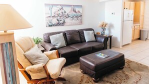 Una sala de estar con sofá, sillón, otomanas y un cuadro en la pared.