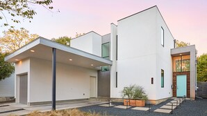 Ein modernes, zweigeschossiges Haus mit Flachdach, großen Fenstern und einer überdachten Auffahrt.
