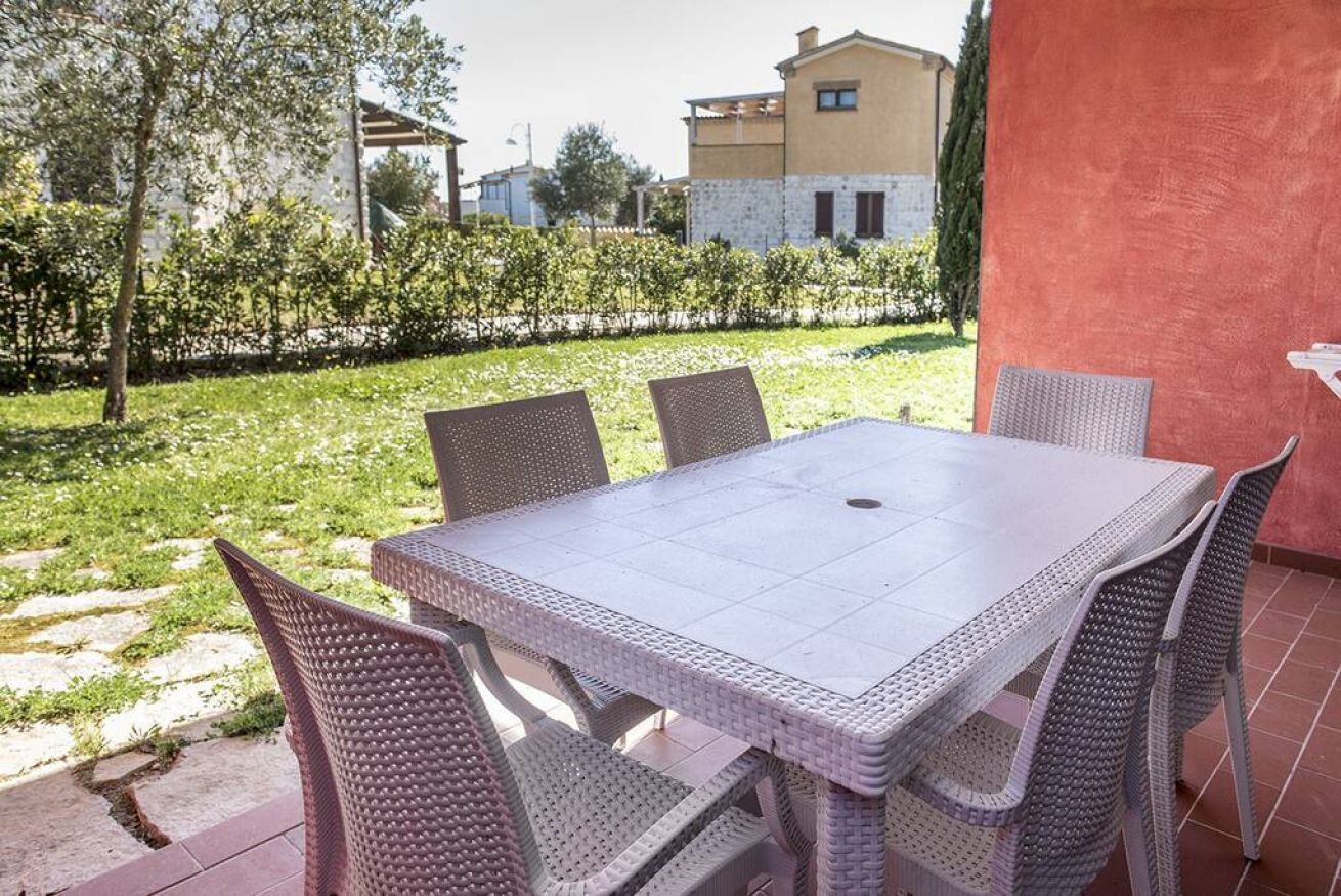 Een terras met tafel en stoelen, omgeven door een tuin en een gebouw.