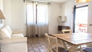 A room with a wooden dining table, white chairs, a sofa, and a window with sheer curtains. - M348 - Marcelli, comfortable new three-room apartment with swimming pool and bal (Numana)